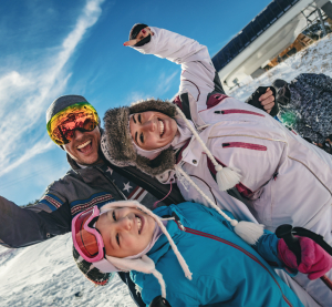 Familie mit Skiklamotten posieren lächelnd auf einer Skipiste