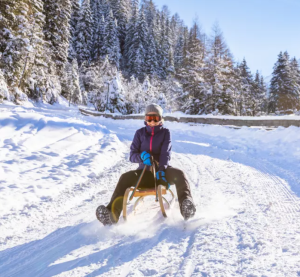 Frau rodelt mit einem Schlitten einen schneebedeckten Berg hinunter